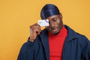 Covering eye, by, credit card. Handsome black man is in the studio against yellow background photo
