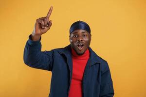 Pointing ,,by the finger to copy space. Handsome black man is in the studio against yellow background photo