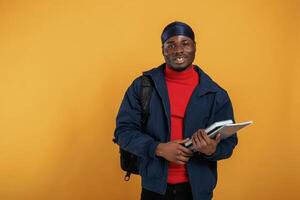 Student with books, backpack, and notepad. Handsome black man is in the studio against yellow background photo