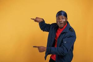 Shocked,, showing something by hand on the wall. Handsome black man is in the studio against yellow background photo