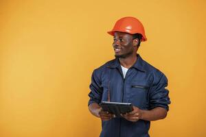 Construction worker ,in, hard hat and with tablet. Handsome black man is in the studio against yellow background photo