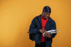 Student, with books, backpack and notepad. Handsome black man is in the studio against yellow background photo