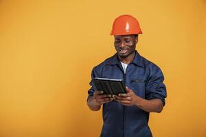 Construction, worker ,in hard hat and with tablet. Handsome black man is in the studio against yellow background photo