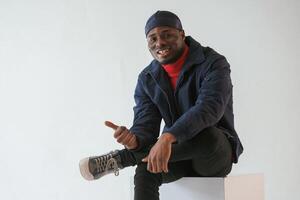 Calm, sitting, smiling and showing thumb up. Black man in cap is in the studio against white background photo