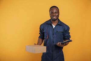 Delivery, service worker with box. Handsome black man is in the studio against yellow background photo