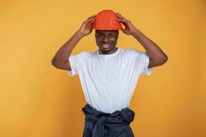 Standing and, posing,, construction worker in hard hat. Handsome black man is in the studio against yellow background photo