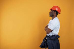 Standing and ,posing, construction worker in hard hat. Handsome black man is in the studio against yellow background photo