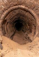 Eerie brick tunnel with pipes and sand leading into darkness photo