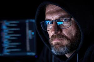 Hacker in hoodie with code reflected in glasses photo