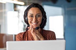Close-up portrait of a woman with a headset, an online customer support worker smiling and looking at the camera, a business woman advising clients, working inside the office, using call. photo