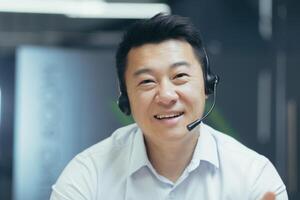 Close-up photo portrait of Asian man with call headset, tech support worker smiling and looking into camera