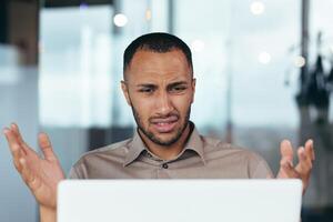 Upset businessman close up looking at laptop screen at work, man unhappy with received email notification, employee disappointed with work result inside office. photo