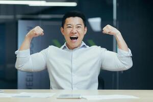 Asian super hero businessman looking at camera and smiling holding hands up gesture of strength and confidence man working in office at work photo