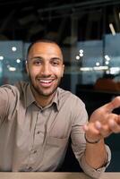 ringing, successful businessman looking at smartphone camera talking remotely with colleagues, Hispanic man smiling at work inside office, webcam view pov vertikal photo