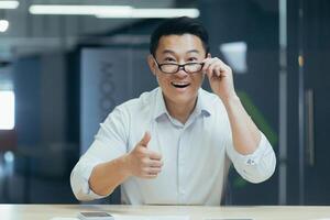 surprised asian man shoots glasses shocked looking at camera. Happy smiling rejoices. Look at monitor screen webcam view. amazed close up portrait. Face Handsome man Office worker wow expression photo