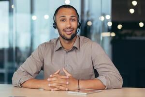 Portrait of a young handsome African American man. He sits in a headset in front of the camera, talks, consults. Business training, webinar, customer support service, online store. photo
