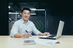 Portrait of asian businessman behind paper work man smiling and looking at camera working in modern office at work photo