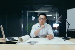Thinking asian engineer architect working in modern design office, man looking at drawing plan. photo