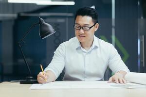 Successful Asian architect works in design studio, on plan drawing of project, makes corrections photo