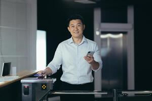 Portrait of an Asian businessman worker, man comes to work for the first time, walks into the office, smiles and looks at the camera at the front door, holds a phone in his hands photo