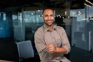 Portrait of african american businessman in office, man in shirt standing near window smiling and looking at camera, programmer working inside development company. photo