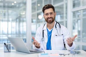 A friendly doctor in a white coat welcomes you in a modern office setting. He is smiling while wearing a stethoscope. photo