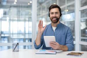 A friendly businessman greets viewers during a call with a smile while holding a tablet in his hands. photo
