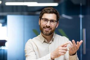 Close-up portrait of a young smiling man sitting in the office in front of the camera, talking on a call, explaining and counting on his fingers. photo