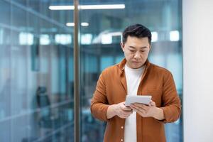 A focused programmer is seen thoughtfully interacting with a tablet device in a modern office setting. photo