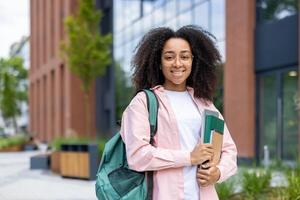 A smiling student stands outside a university building, carrying books and a backpack. Her cheerful expression suggests academic success and a positive attitude. photo