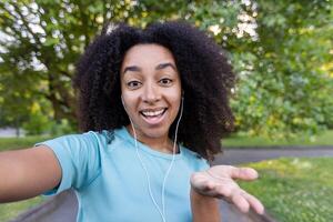 Smiling woman enjoying active fitness routine outdoors, using phone for call. Her cheerful expression reflects joy and connection, as she wears headphones in an outdoor park setting photo