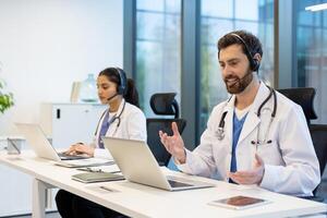 Two doctors working remotely consulting patients remotely, man and woman with headset using laptop for call, working inside clinic, patient support and assistance service. photo