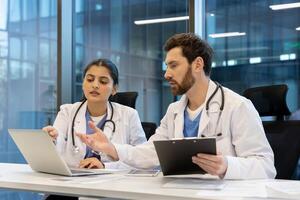 Two medical professionals collaborate, discussing information displayed on a laptop in a modern office setting. They are reviewing data together. photo