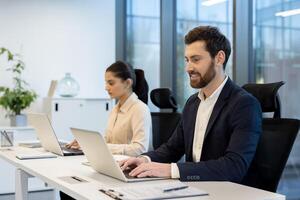 A diverse team works collaboratively in a modern office setting, focusing on their laptops with expressions of concentration. photo