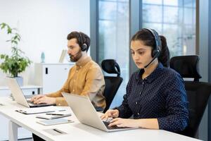 Two customer service representatives are working diligently at their computers, wearing headsets, in a modern office environment. photo