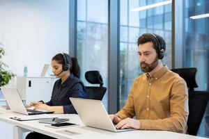 Two customer service representatives working in a modern office environment, each using laptops and headsets. photo