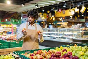 A grocery store employee carefully inspects a pair of apples in the produce section, evaluating their quality. photo