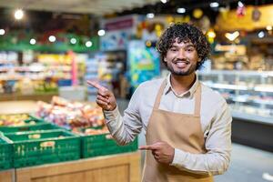 A smiling grocery store employee points to the fresh produce section, offering a friendly and inviting experience for customers in this environment. photo