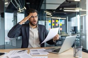 Upset and disappointed financier working on paperwork, man dissatisfied with performance results. Businessman checking bad financial reports and contracts. photo