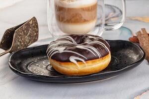 A donut on a plate with a cup of coffee and a spoon photo
