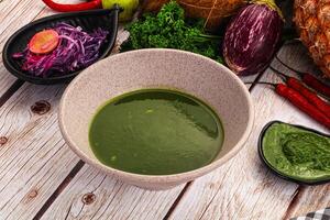 A bowl of green sauce on a table next to a pineapple photo