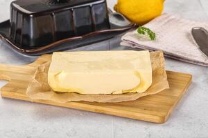 A piece of butter on a cutting board next to a knife and a lemon photo
