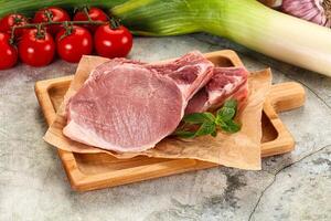 Raw pork chops on a cutting board with tomatoes and vegetables photo