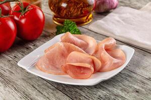 A plate of sliced ham on a table with tomatoes and other ingredients photo