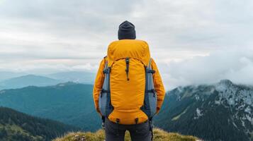 hiker stands on mountain edge, gazing at vast landscape with yellow backpack photo