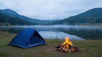 Camping by serene lake with glowing campfire and misty mountains background evokes tranquility photo