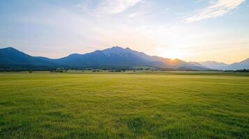 Serene landscape featuring vast green field with distant mountains under warm sunset glow photo