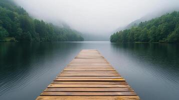Serene wooden dock extends into misty lake surrounded by lush green trees, creating tranquil photo