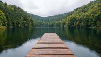 Serene lake view with wooden dock surrounded by lush green forests and mountains photo