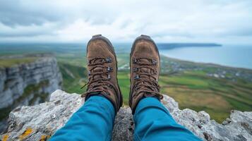 A person wearing hiking boots sitting on a rock overlooking the ocean photo